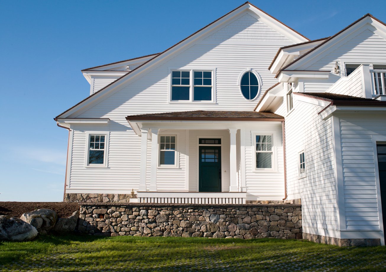 A classic coastal cottage with white siding and Andersen® 400 Series windows, including an oval shaped specialty window.