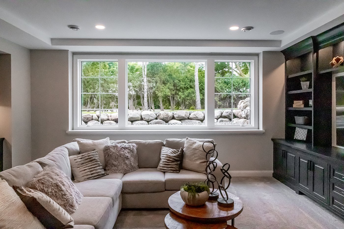 A basement living room with a row of three windows, built-in cabinetry, and a sectional and coffee table.