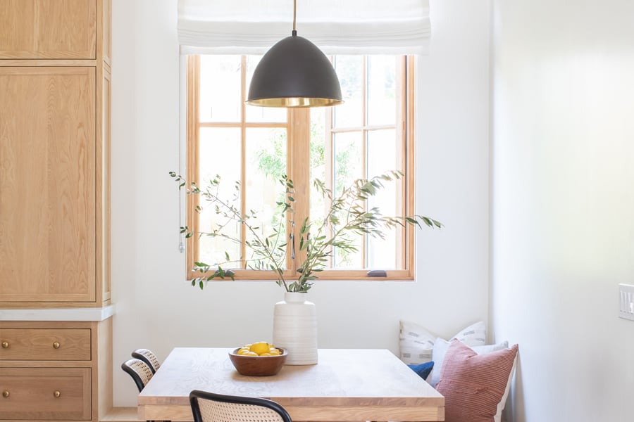 A kitchen with white walls and warm white oak cabinetry and built-in benches lit by a twin Andersen® E-Series Casement Window with white oak frames.