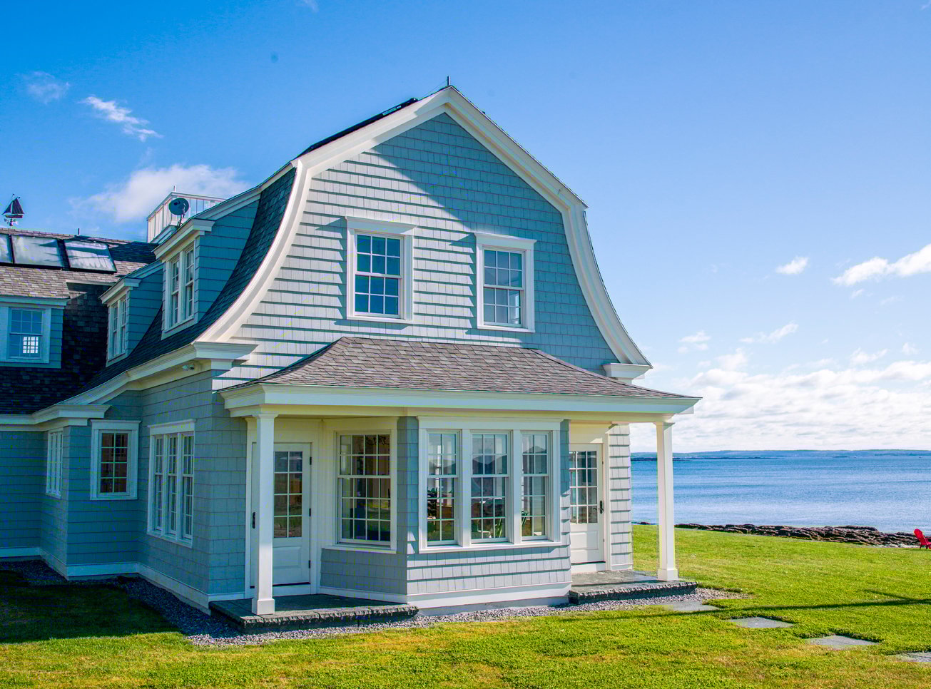 A seaside home with cedar shakes and white Andersen® E-Series Double-Hung Windows with a colonial grille pattern and cottage sashes.