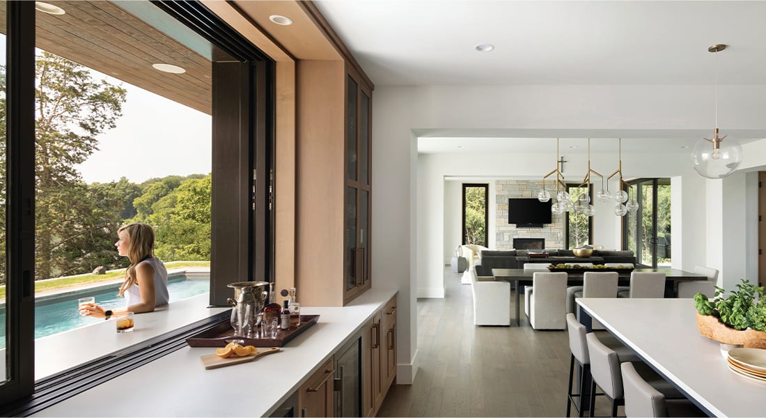 A woman sits outside a Pass-Through Window connecting a pool area with a kitchen.