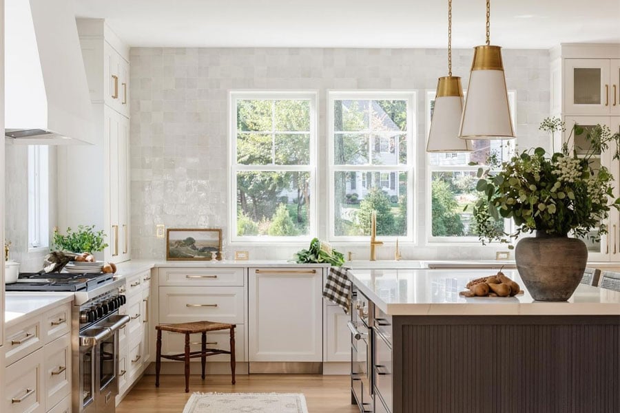 A kitchen with white zellige tile, a large wood island, and a bank of three white windows above the sink.