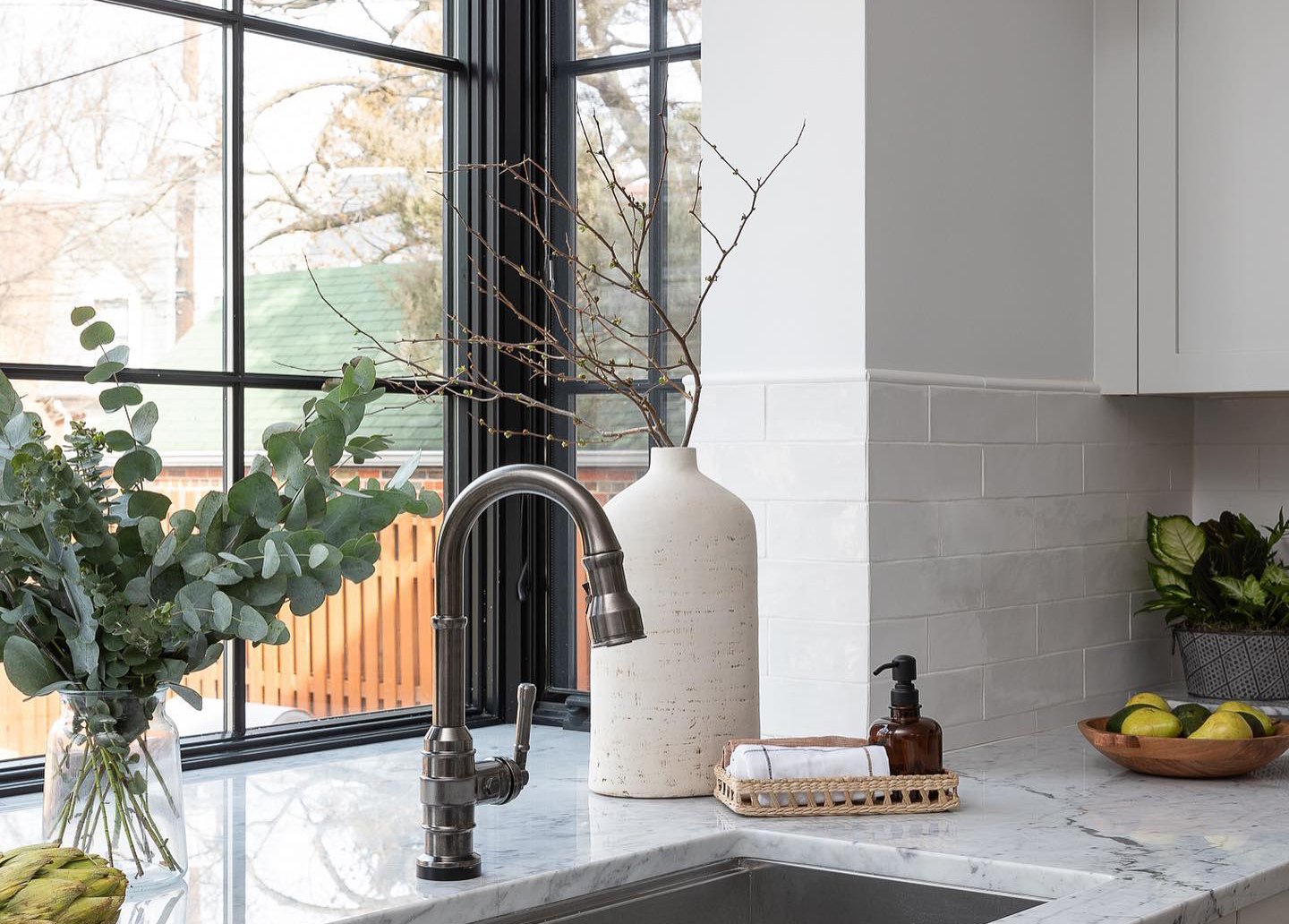 A garden window with black frames and colonial grilles in a kitchen with marble countertops and subway tile.