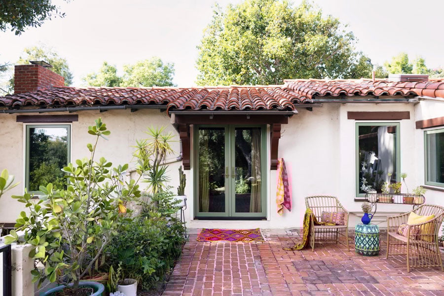 A seating area in a corner of a brick courtyard with two chairs and potted plants outside a set of two E-Series Casement Windows in olive green.