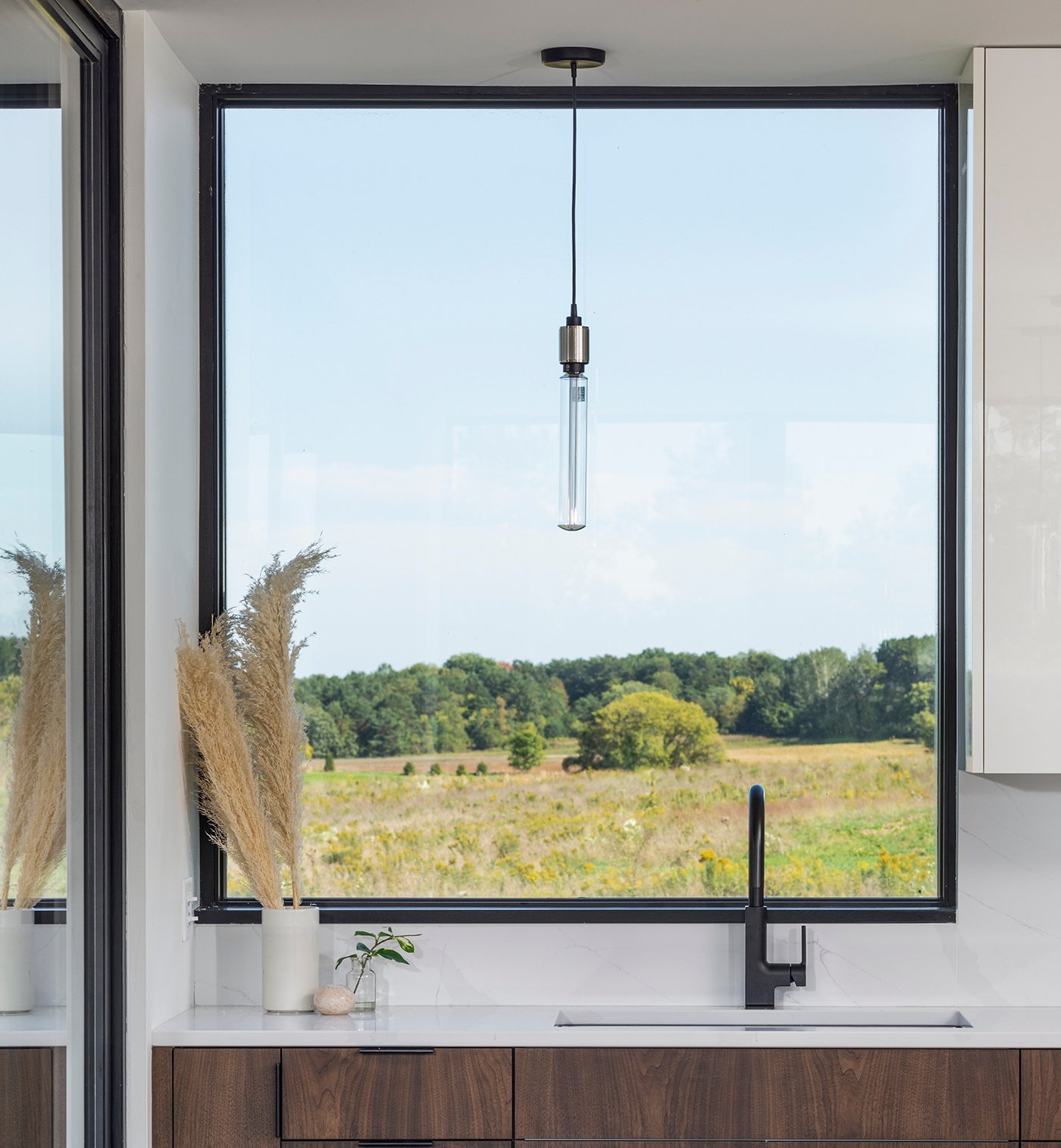 A kitchen sink with a large E-Series Picture Window above it framing a rolling prairie in bloom.