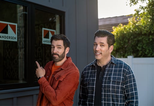 Drew and Jonathan Scott standing in front of new home with Andersen Windows stickers on the windows