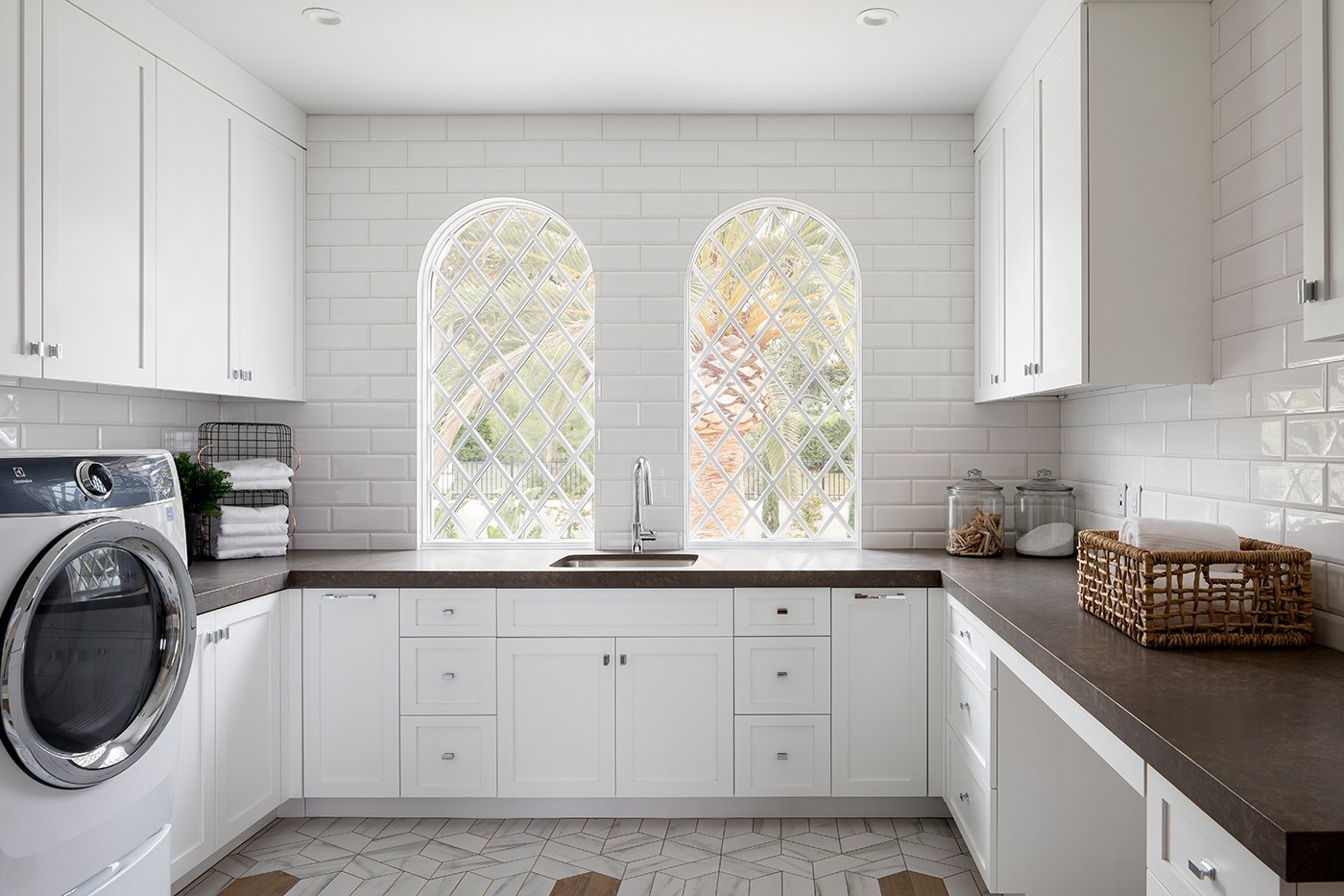 A laundry room with white cabinetry and tile and two Andersen® E-Series Springline™ Windows behind the sink.