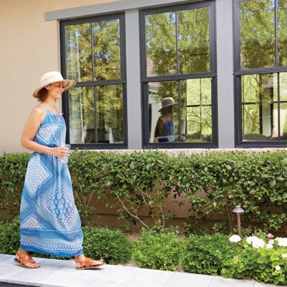 Woman in sun dress walking on sidewalk next to windows with grilles